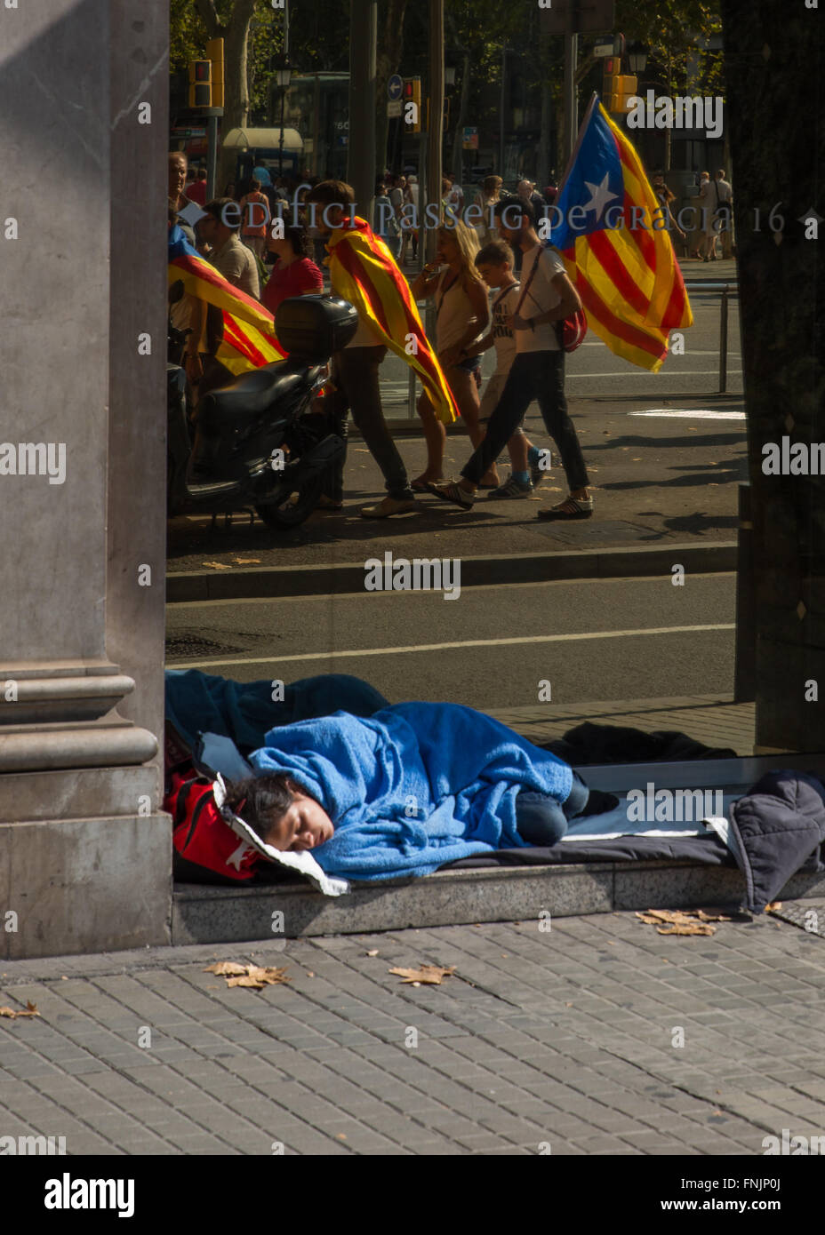 Sep 11, 2015 - Barcellona, Spagna - senzatetto donna dorme in una banca porta come persone marzo indossando la bandiera catalana all'Arc de Triomf di Barcellona. Barcellona è stato un mare di rosso e giallo come la folla portando bandiere separatisti hanno marciato in città per celebrare il catalano Giornata Nazionale. Gli organizzatori spera di attirare almeno mezzo milione di persone per un pro-indipendenza rally usando lo slogan 'cominciamo a costruire un nuovo paese". La Estelada o "Lone Star bandiera" è una Bandiera non ufficiale tipicamente percorse da catalano separatisti per esprimere il loro sostegno ad un organismo indipendente la Catalogna. (Credito Immagine: © Ruaridh Stewart/ZUM Foto Stock
