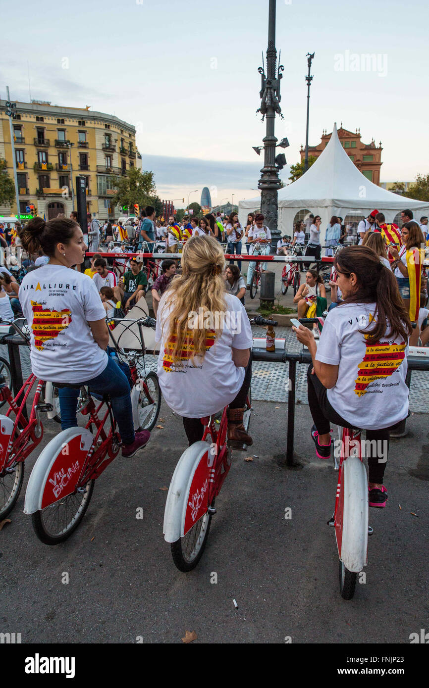 Sep 11, 2015 - Barcelona, Spagna - 3 donne siedono sul noleggio biciclette indossando proposto mappa Catalonia sulle camicie. Persone marzo indossando la bandiera catalana all'Arc de Triomf di Barcellona. Barcellona è stato un mare di rosso e giallo come la folla portando bandiere separatisti hanno marciato in città per celebrare il catalano Giornata Nazionale. Gli organizzatori spera di attirare almeno mezzo milione di persone per un pro-indipendenza rally usando lo slogan 'cominciamo a costruire un nuovo paese". La Estelada o "Lone Star bandiera" è una Bandiera non ufficiale tipicamente percorse da catalano separatisti per esprimere il loro sostegno ad un organismo indipendente la Catalogna. (Credi Foto Stock