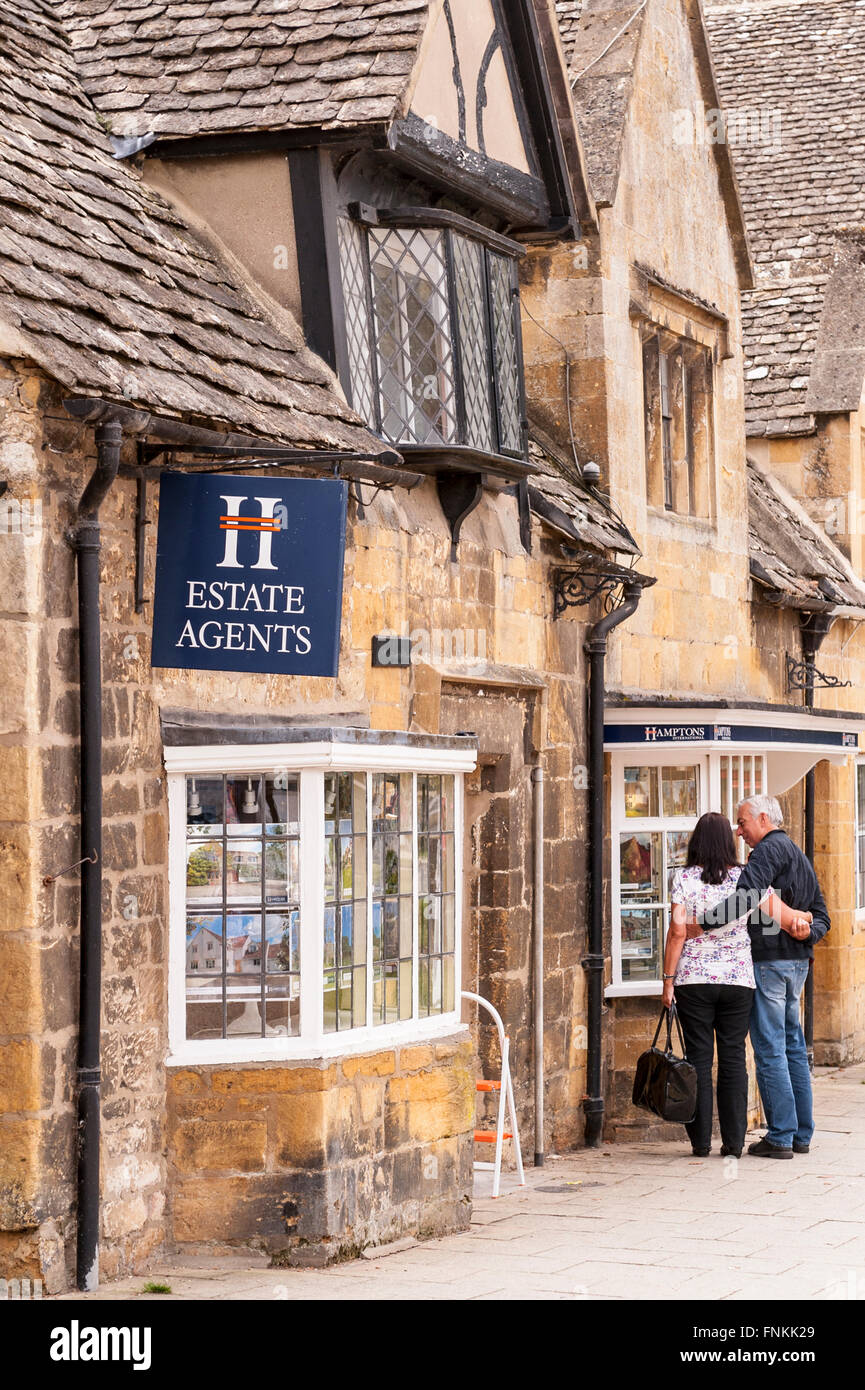 Una coppia in cerca di un Agenti Immobiliari finestra in Broadway , Worcestershire , Inghilterra , Inghilterra , Regno Unito Foto Stock