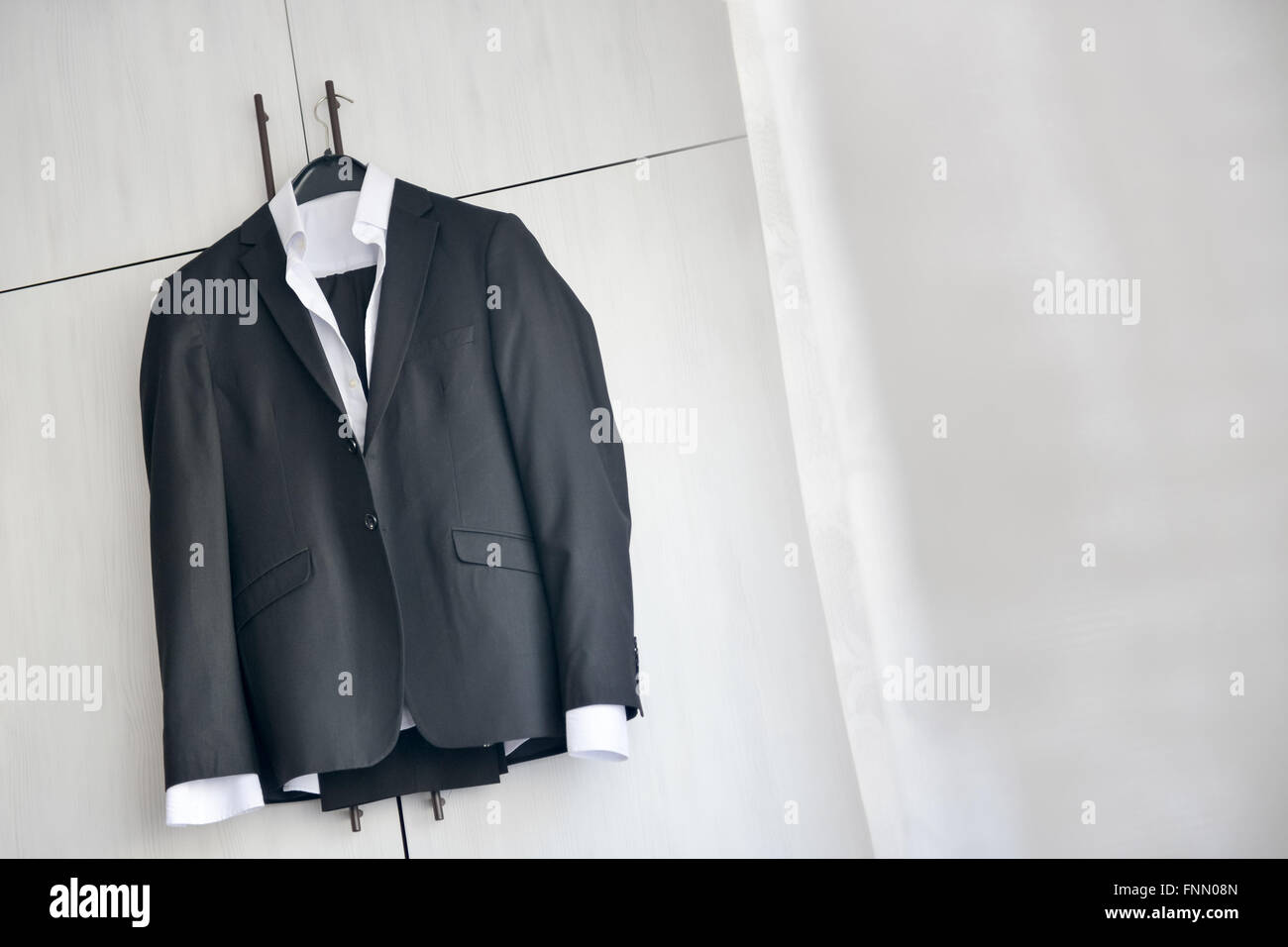 Abito nero appeso ad un armadio in legno nella luce naturale Foto Stock