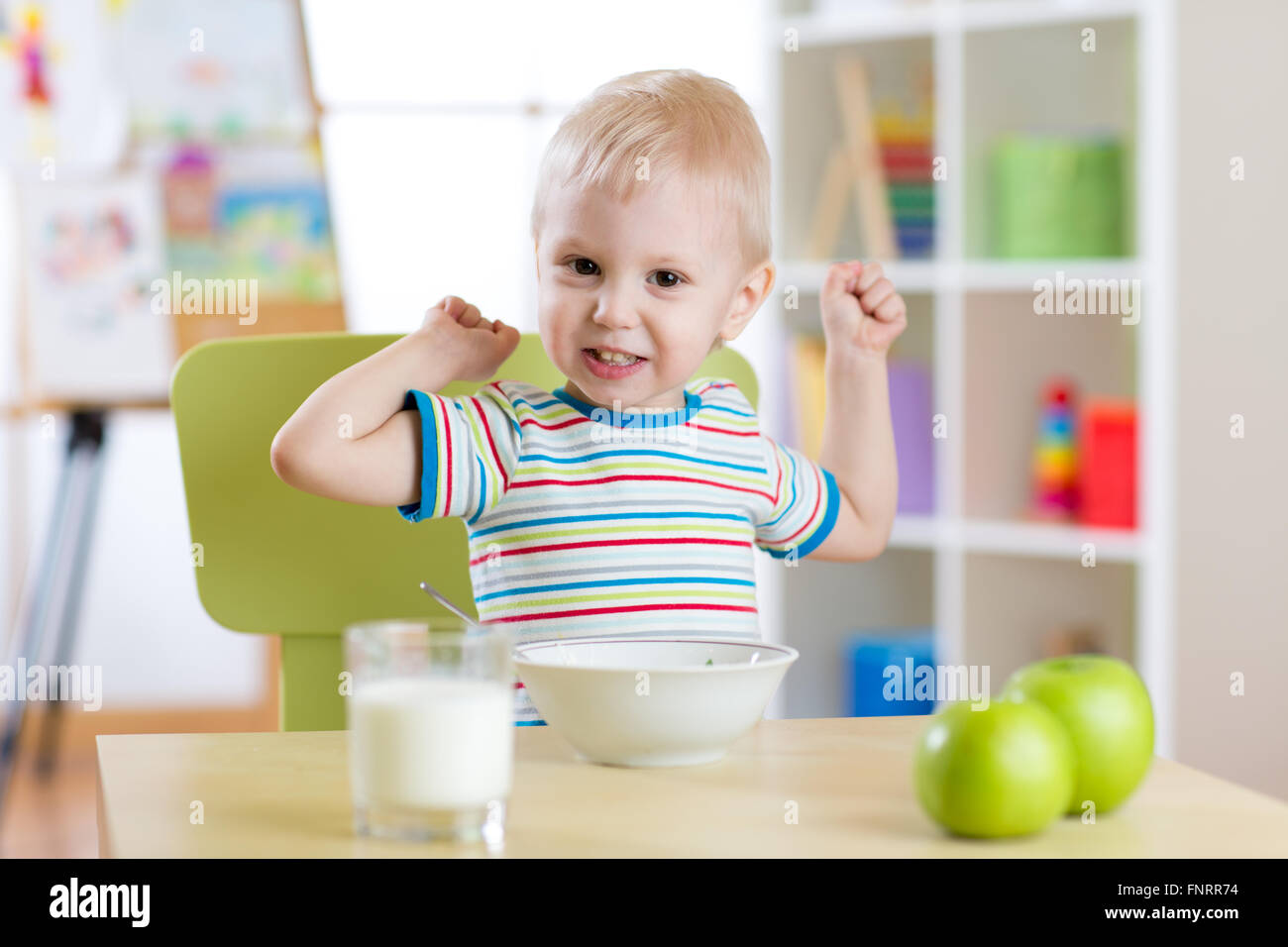 Bambino ragazzo di mangiare cibo sano e che mostra la sua forza in ambienti interni Foto Stock