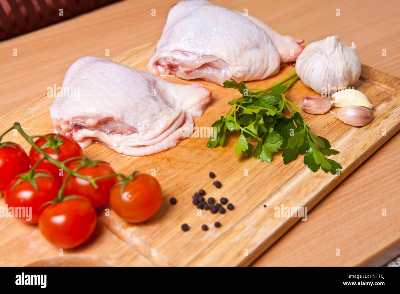 Materie le cosce di pollo con spezie e verdure su un tagliere Foto Stock