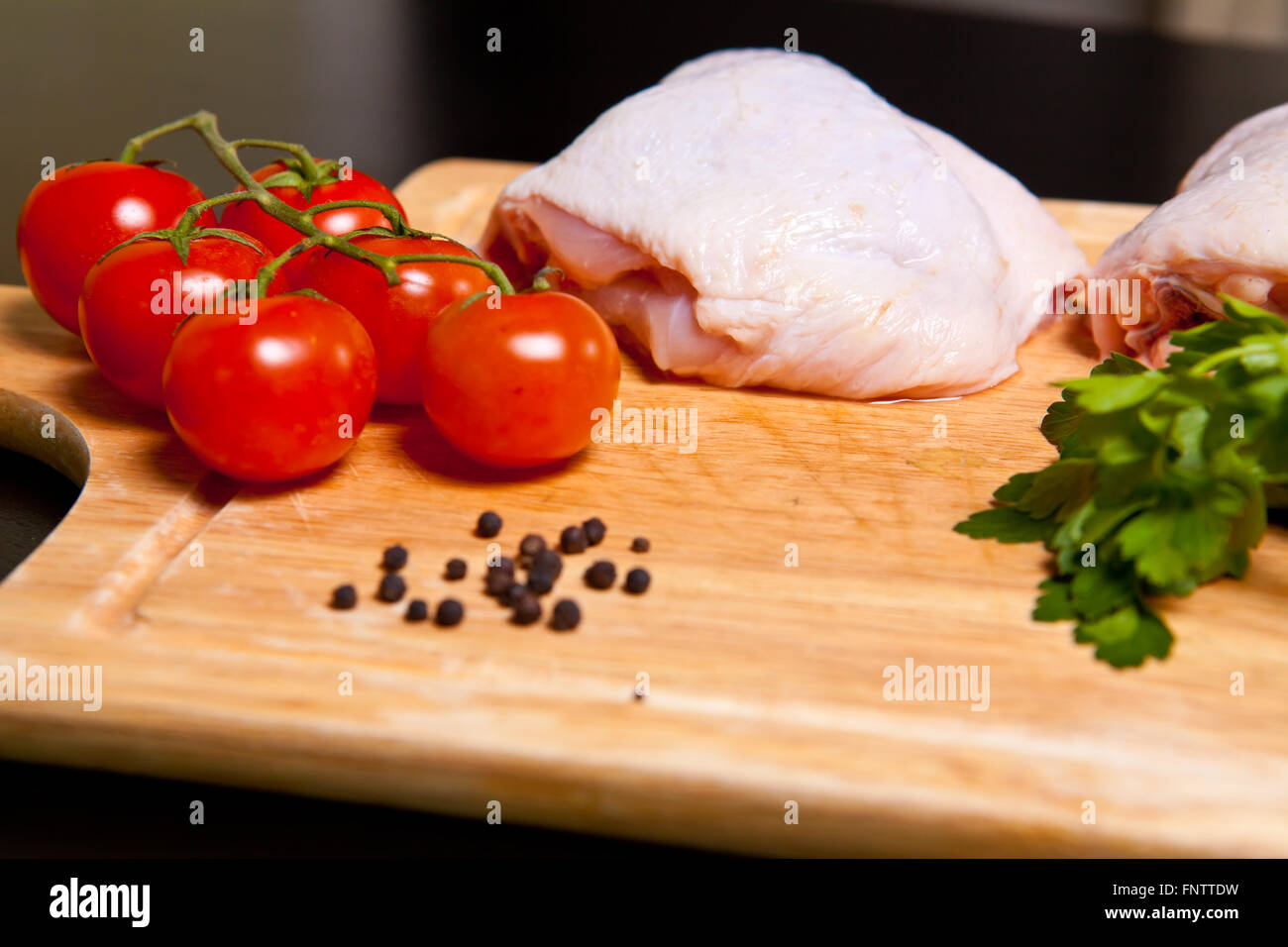Materie le cosce di pollo con spezie e verdure su un tagliere Foto Stock