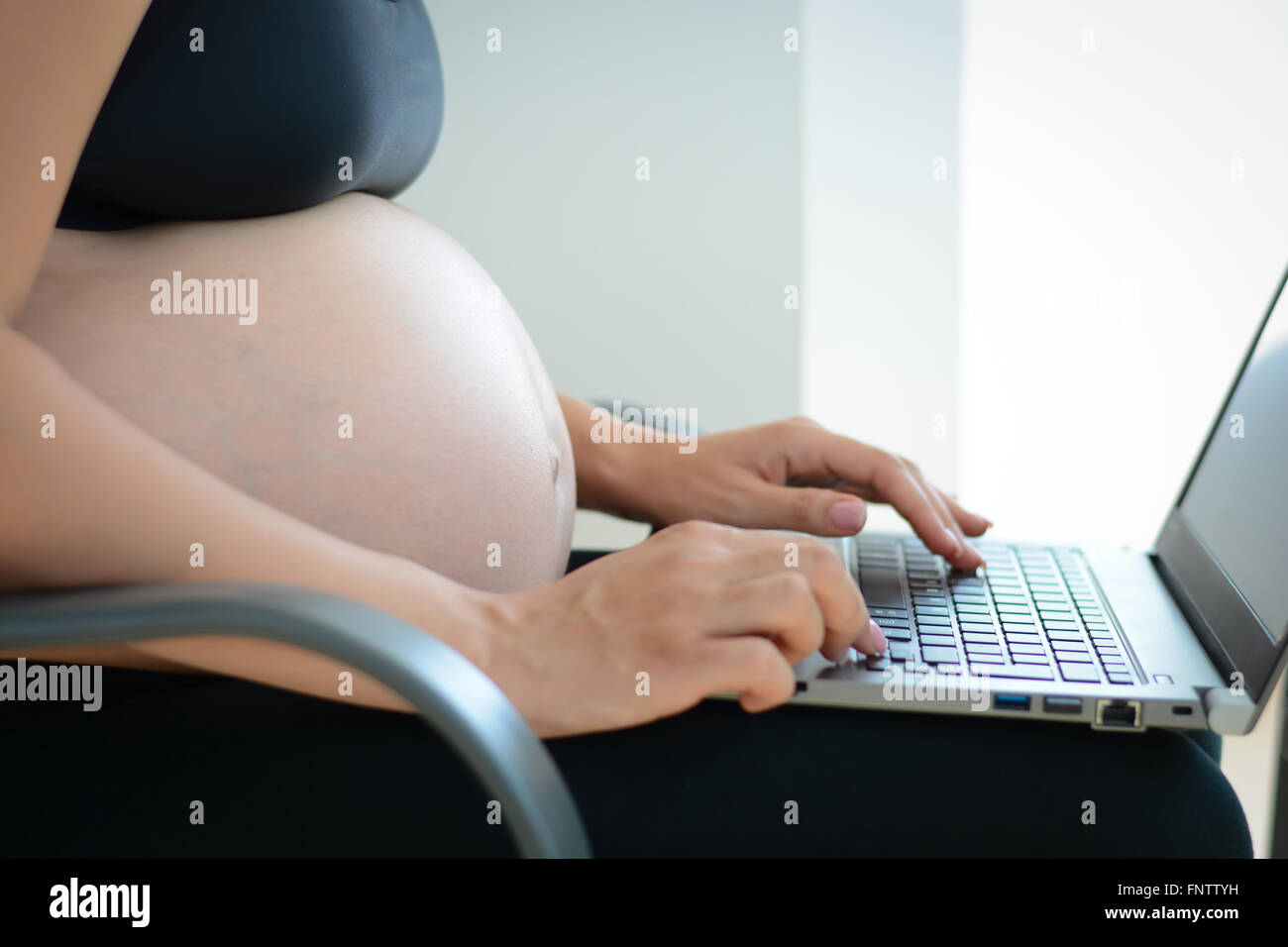 Giovane donna incinta usando un computer portatile a casa Foto Stock