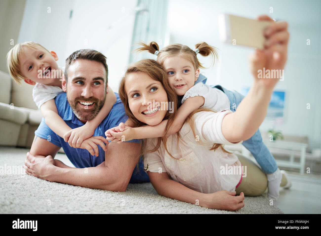 Felice famiglia giovane tenendo selfie sul pavimento a casa Foto Stock