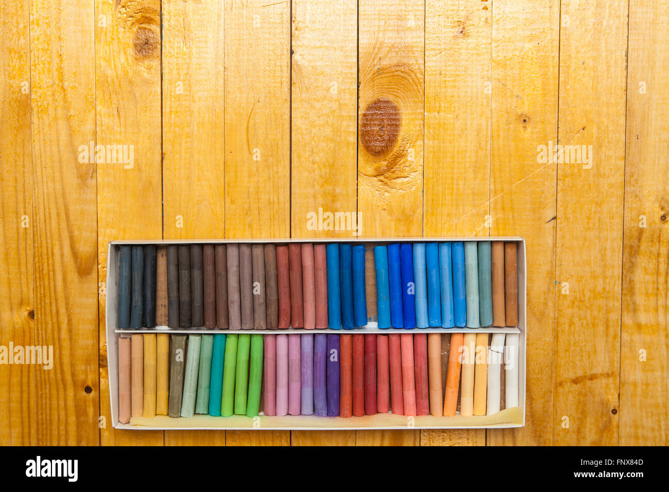 Pastelli colorati in una casella su un sfondo di legno Foto Stock