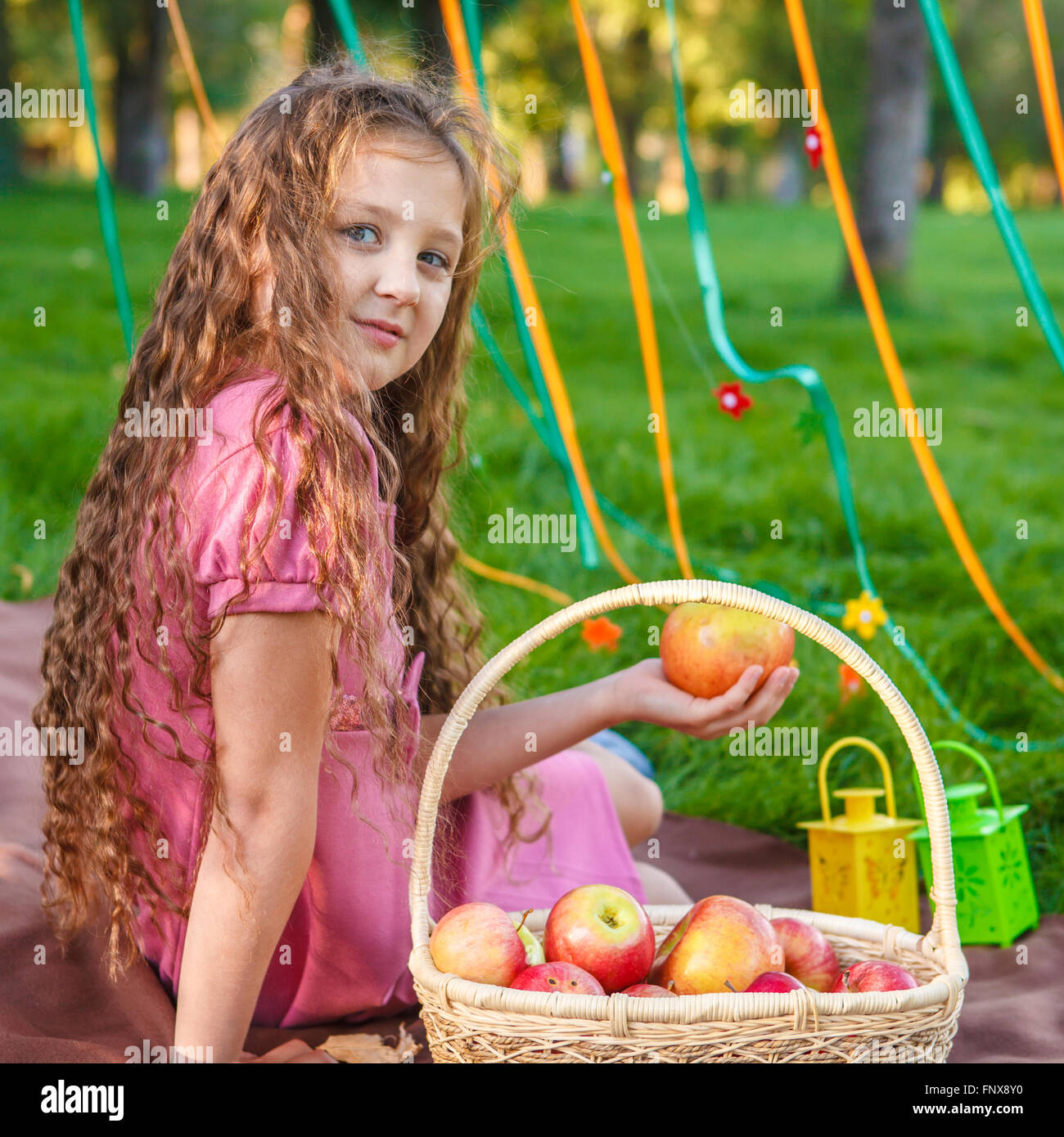Ragazza seduta sul plaid nel parco con un cesto di mele Foto Stock