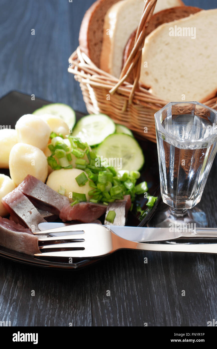 La piastra nera con aringa e patate vicino un bicchiere di vodka Foto Stock