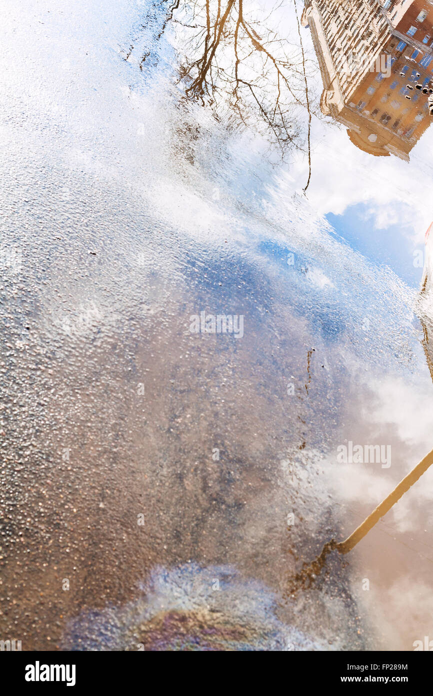 Pozzanghera con case di riflessi e macchie di olio motore sul pavimento bagnato nella giornata di primavera Foto Stock