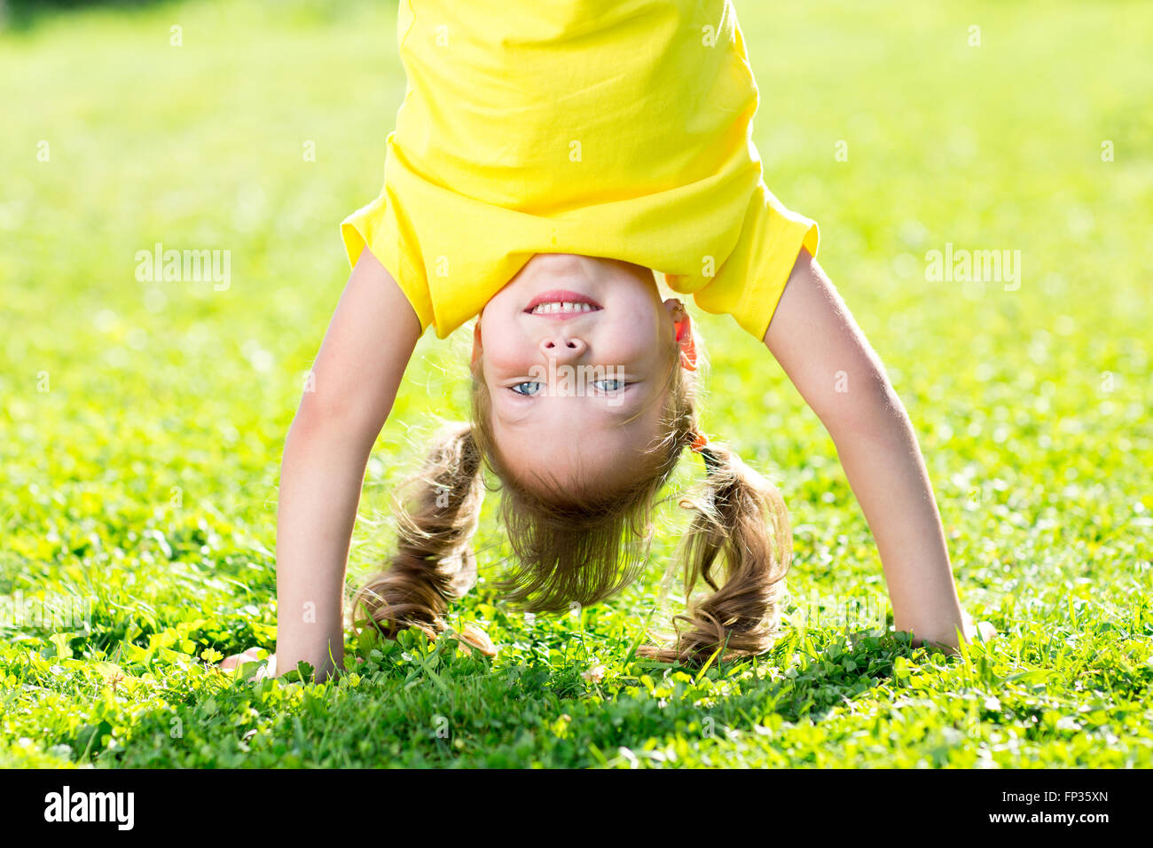 Kid girl standing capovolto sul suo capo su erba in estate Foto Stock