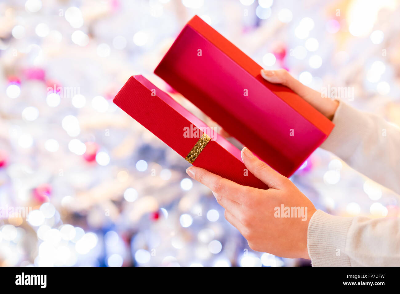 La donna si apre un regalo rossa nella parte anteriore di un albero di Natale Foto Stock