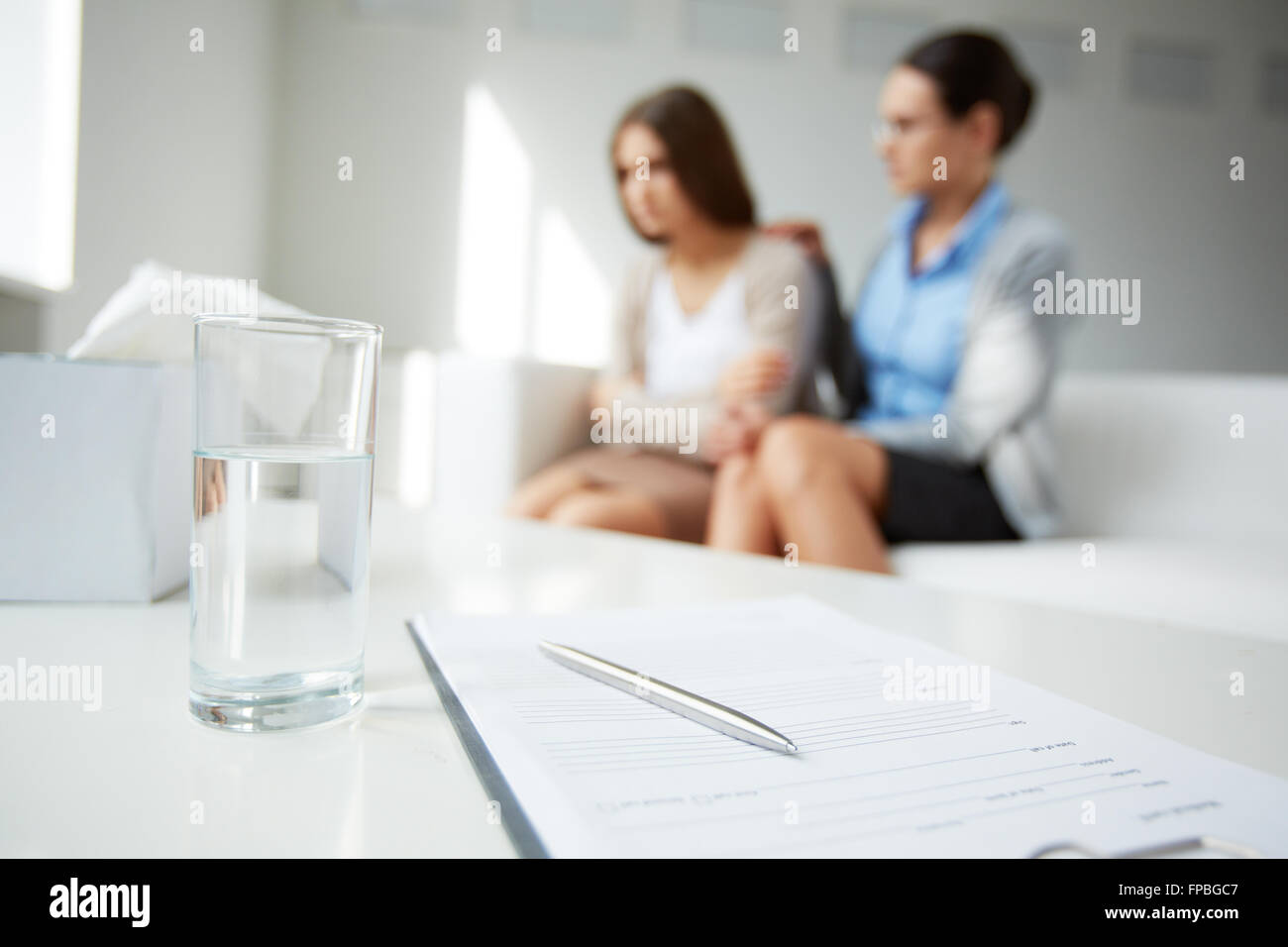 Bicchiere di acqua con documenti sul tavolo con persone in background Foto Stock