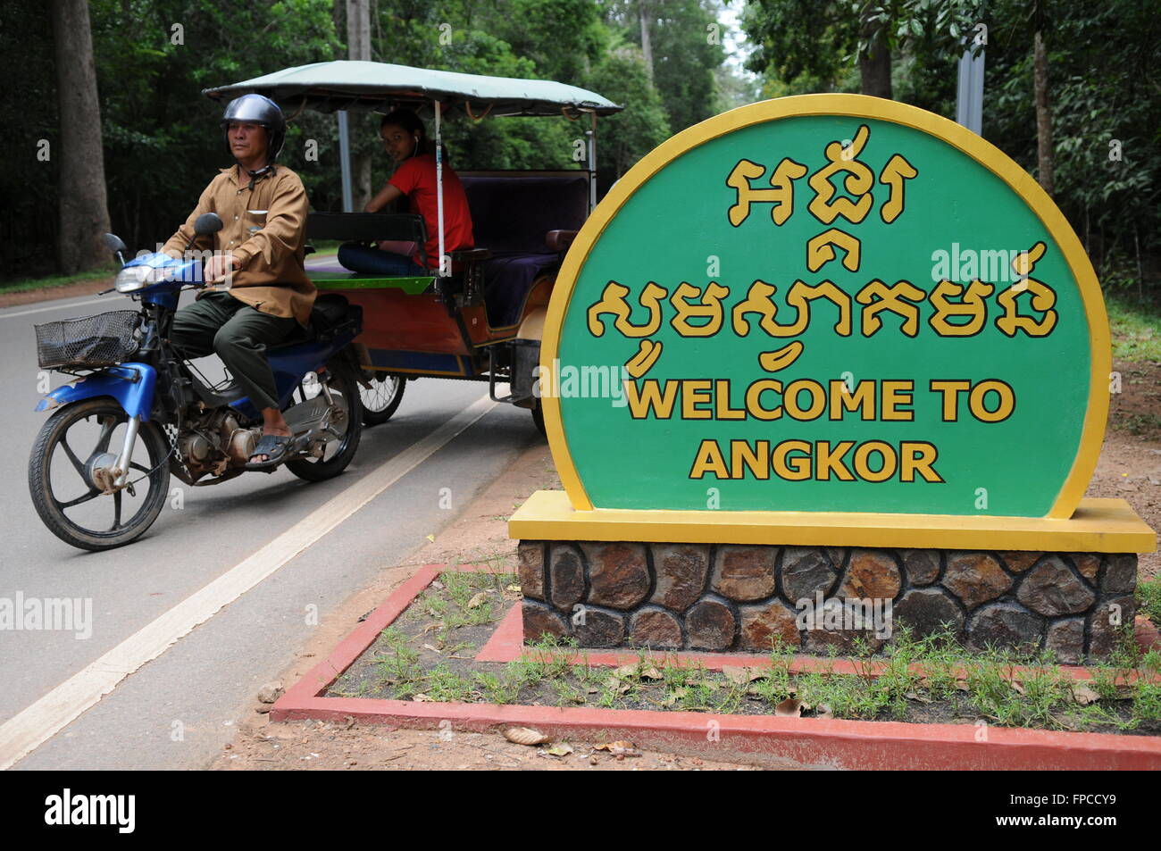 Un Tuk Tuk o remork attende vicino al 'bilingue Benvenuto a Angkor' firmare (sia in inglese e Khmer), Siem Reap Provincia, Cambogia. Credito: Kraig Lieb Foto Stock