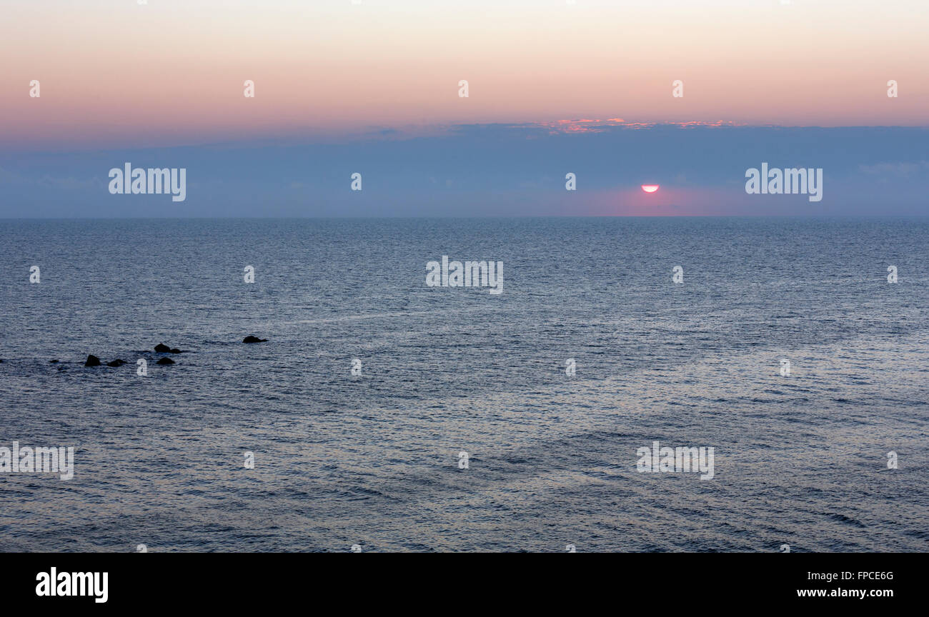 Sunrise scenario del mare con sole nel cielo e cime di rocce sottomarine al di sopra dell'acqua. Foto Stock