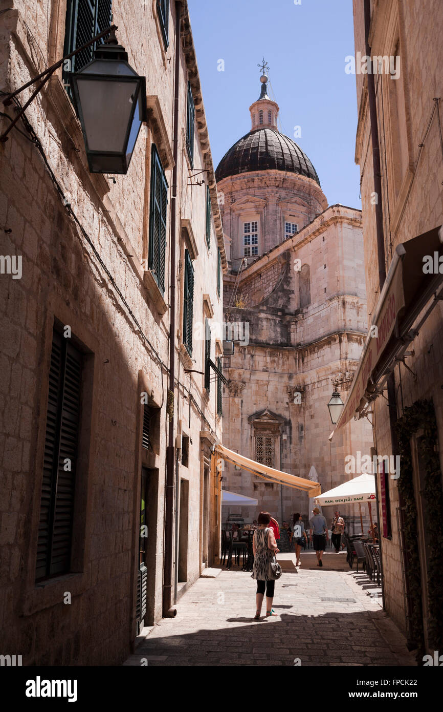 Una donna si erge tra due edifici antichi in una stretta strada di Dubrovnik, con una chiesa o una moschea nella parte inferiore. Foto Stock
