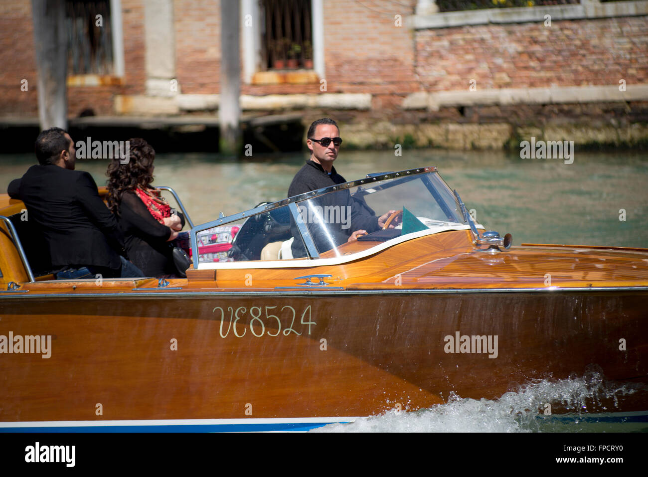 Barca-taxi skipper in una riva boat con due passeggeri sul Canal Grande di Venezia su una soleggiata giornata di primavera Foto Stock