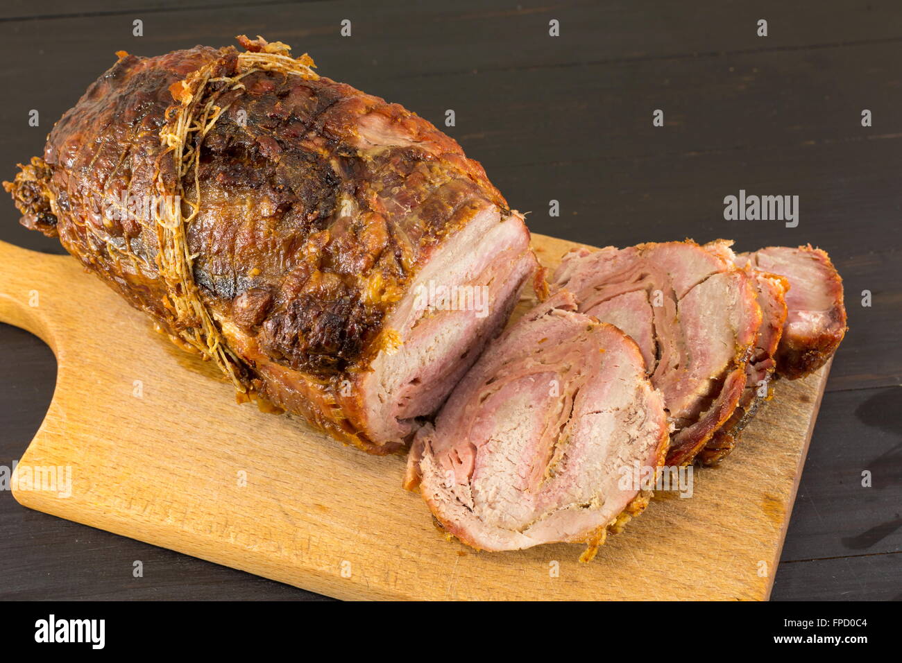 Arrosto di maiale arrotolata la carne su un tagliere su una tavola nera Foto Stock