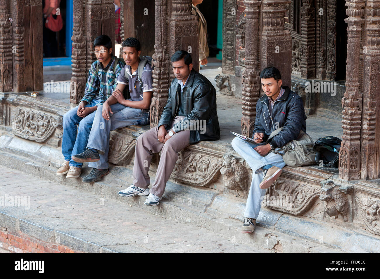 Il Nepal, Patan. Giovani nepalesi uomini appendere fuori a Vishwanath Mandir. Il tempio di Vishwanath sopravvissuto al terremoto del 2015. Foto Stock