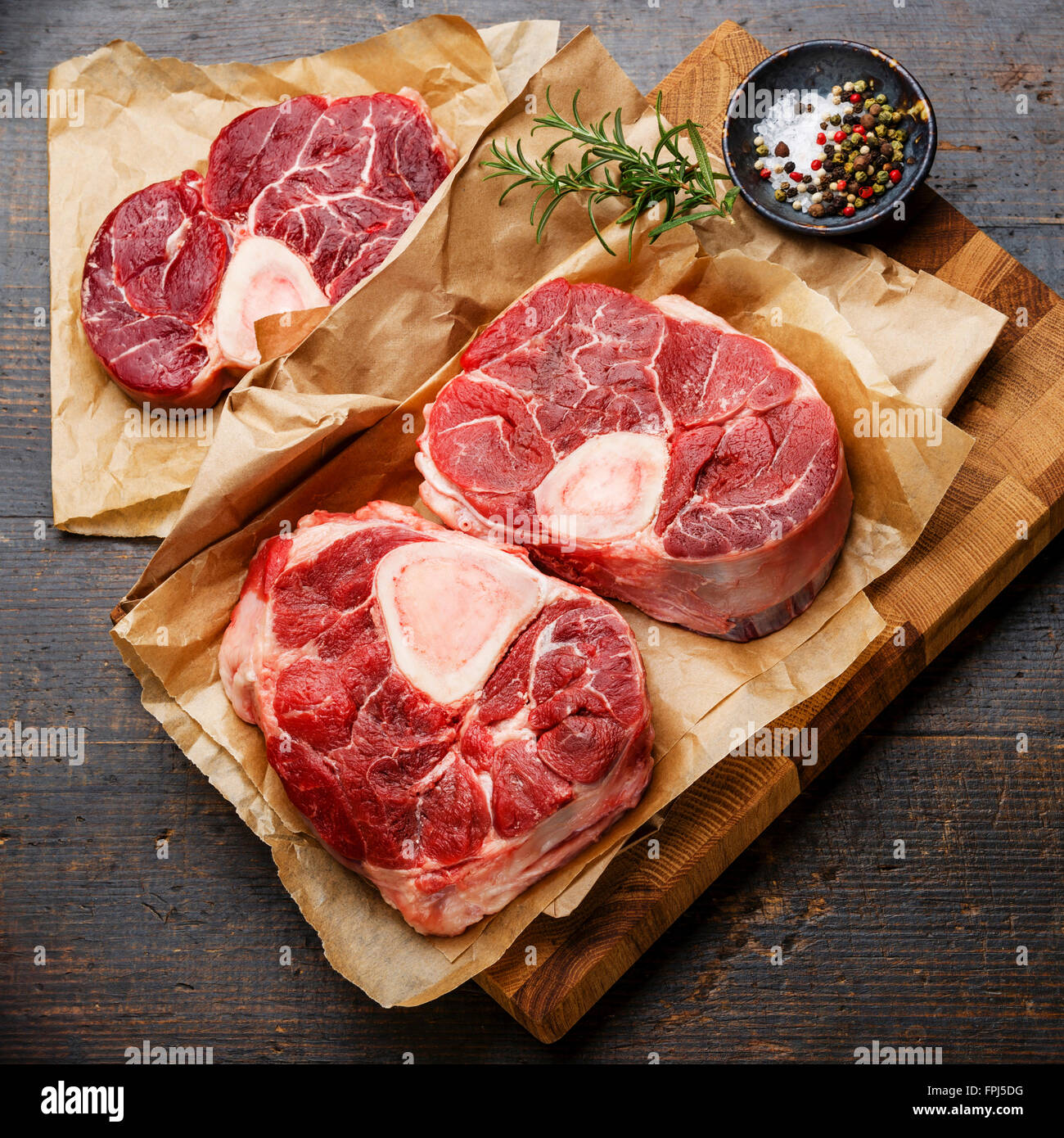 Crudo fresco di taglio trasversale di Stinco di vitello e condimenti per la produzione di Osso Buco sul tagliere di legno Foto Stock