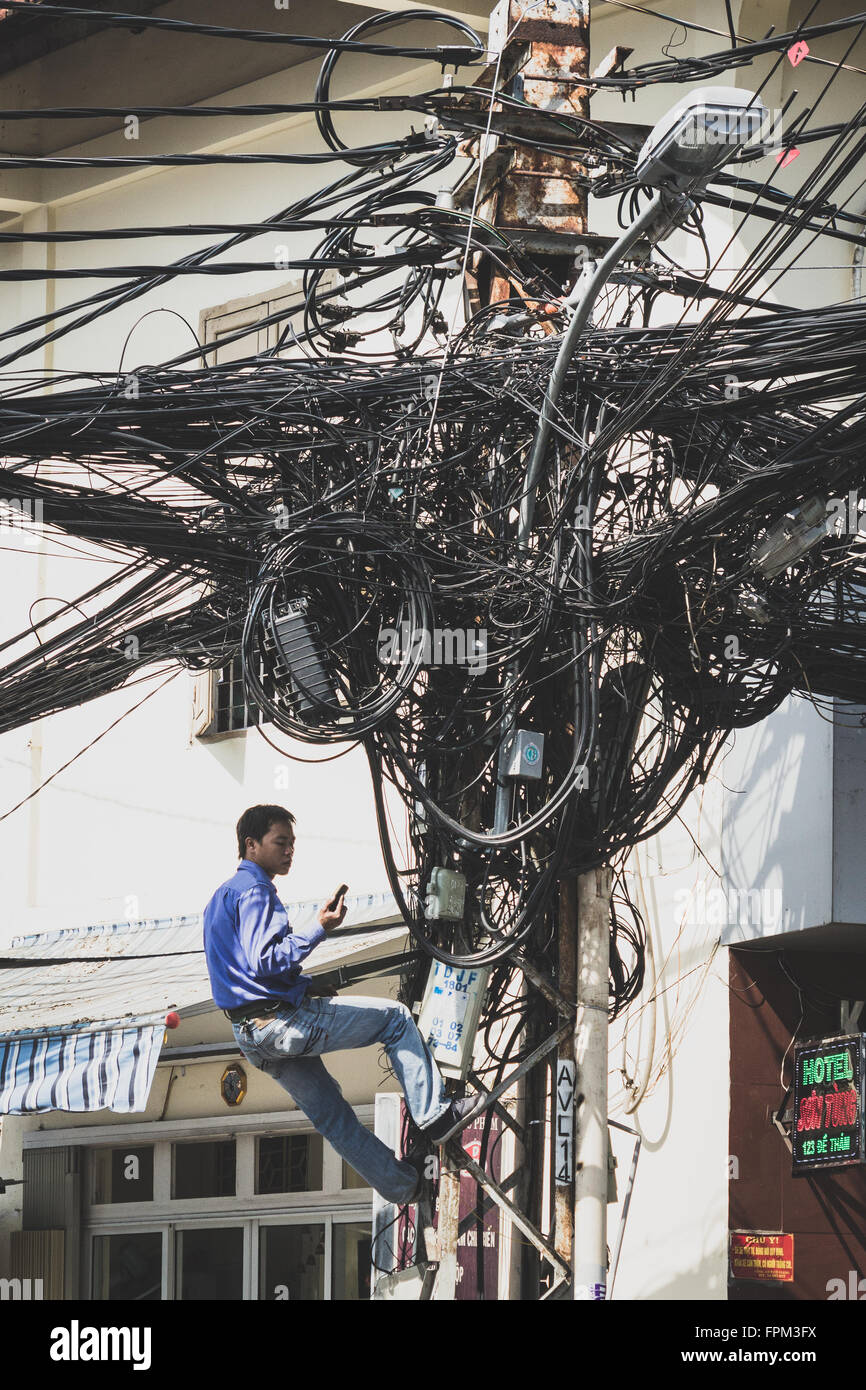 A Saigon, Vietnam - 20 Gennaio 2014: Elettricista fissaggio cavi disordinati sul montante del telefono. Foto Stock