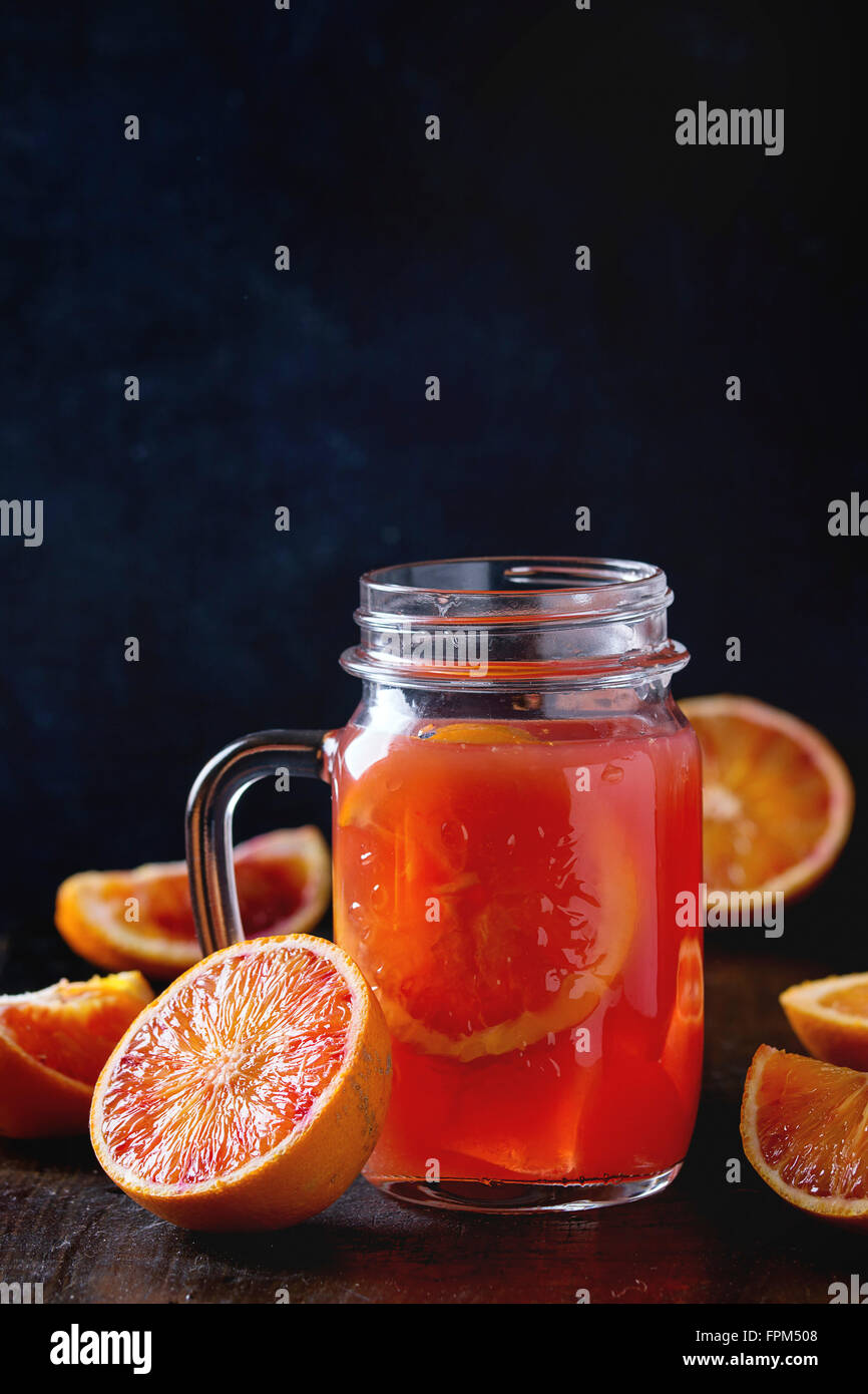 Tagliate a fette il sangue siciliano arance e vetro mason jar di rossi freschi succhi di arancia sopra il vecchio tavolo in legno. Scuro in stile rustico. Foto Stock