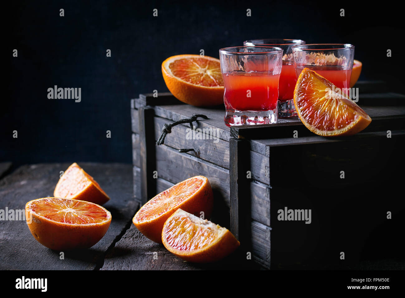 Pantaloncini corti di alcol cocktail con fette di sangue siciliano di arance e rossi freschi succhi di arancia, servita su nero cassa di legno sopra il vecchio Foto Stock