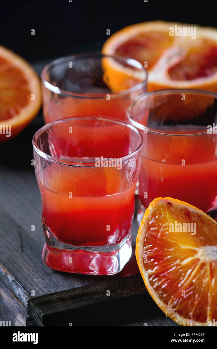 Close up di corti di alcol cocktail con fette di sangue siciliano di arance e rossi freschi succhi di arancia, servita su nero sulla scheda di legno Foto Stock