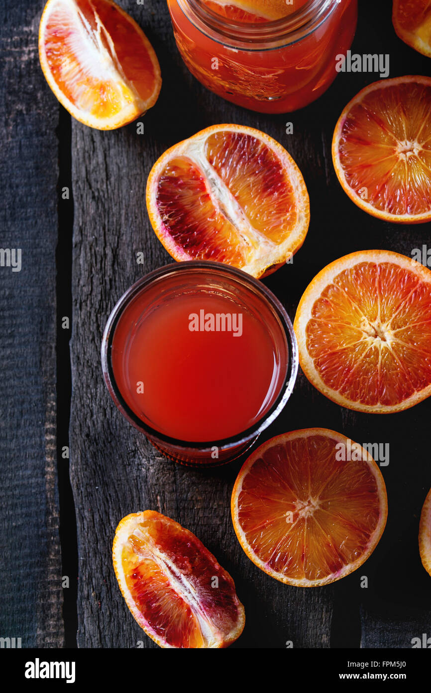 Affettato siciliano di arance sanguigne in turchese piastra in ceramica e vetro di rossi freschi succhi di arancia sopra il vecchio tavolo in legno. Rustico scuro Foto Stock