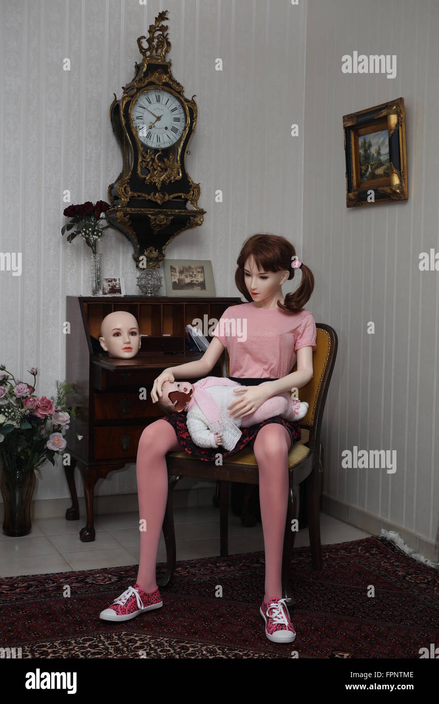Bambola di silicone seduti su una sedia e la holding Fantoccio rotto con la metà di una faccia, fotografato a Colonia, Germania Foto Stock