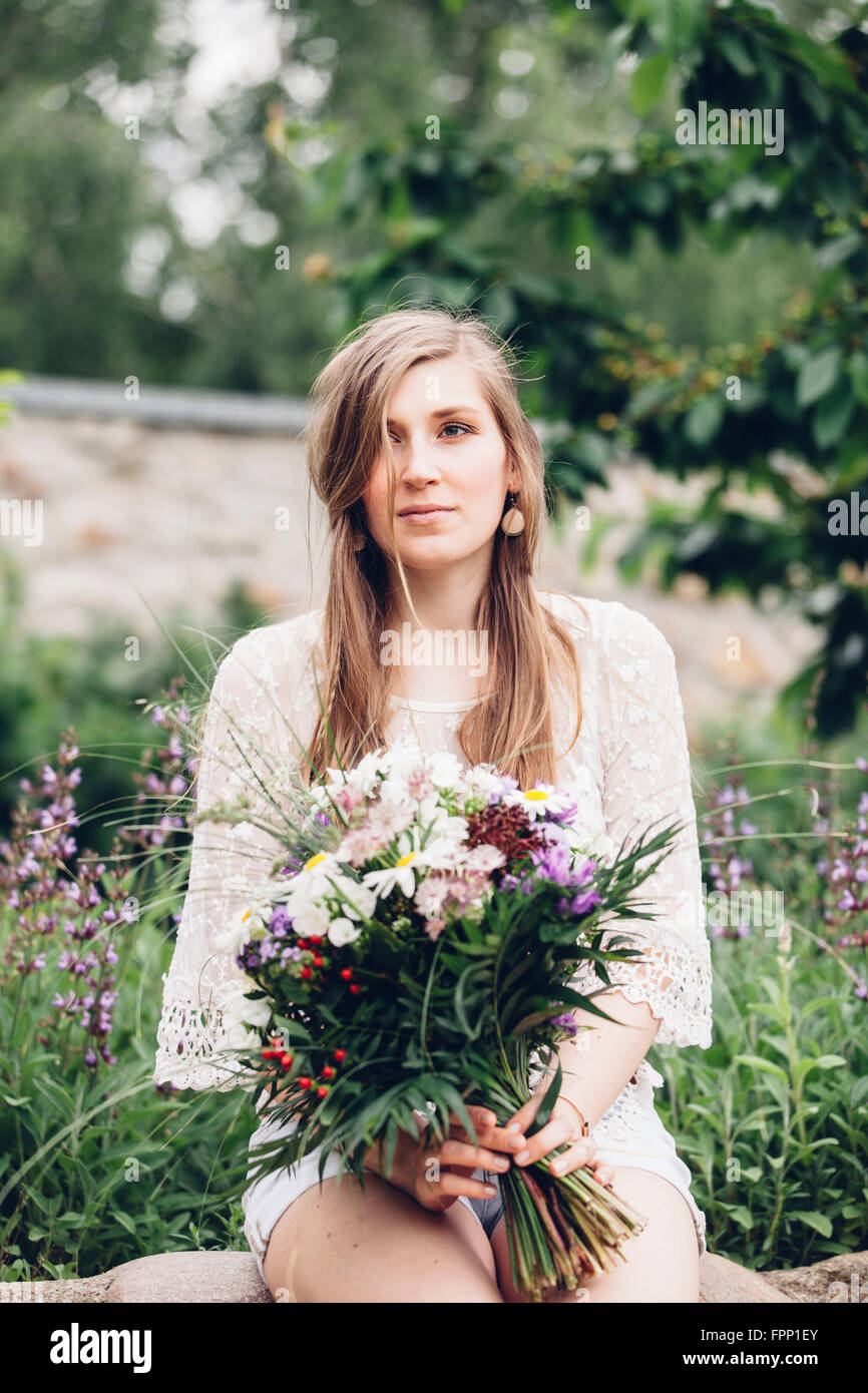 Giovane donna seduta con fiori nel giardino, Foto Stock