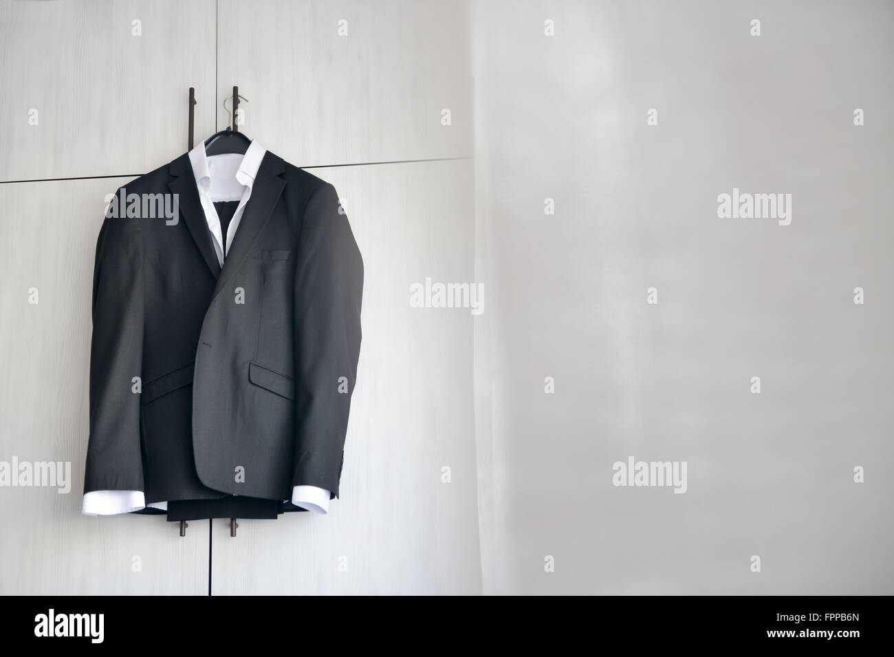 Abito nero appeso ad un armadio in legno nella luce naturale Foto Stock