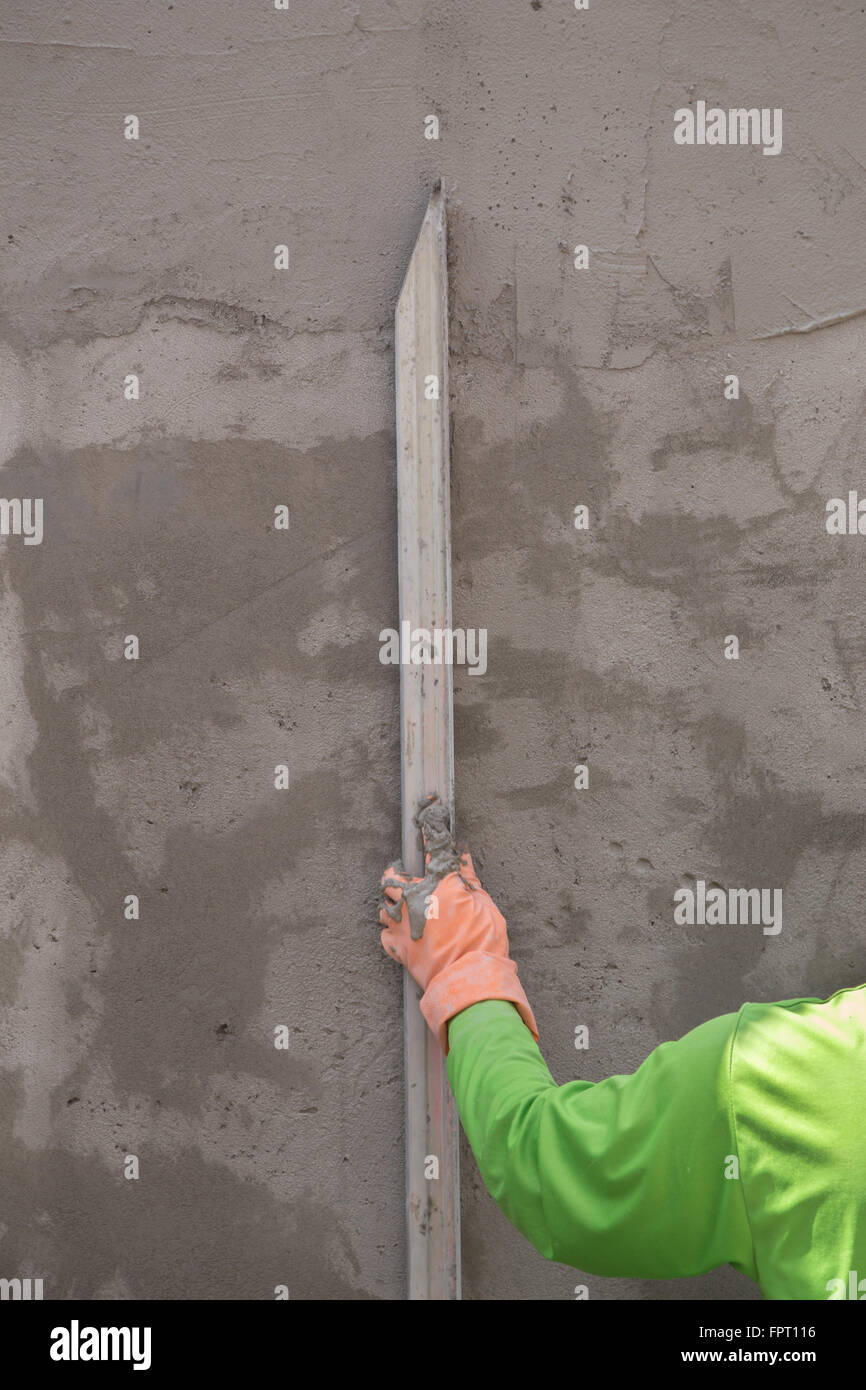 Stretta di mano con cazzuola per finire di calcestruzzo bagnato muro al sito in costruzione Foto Stock