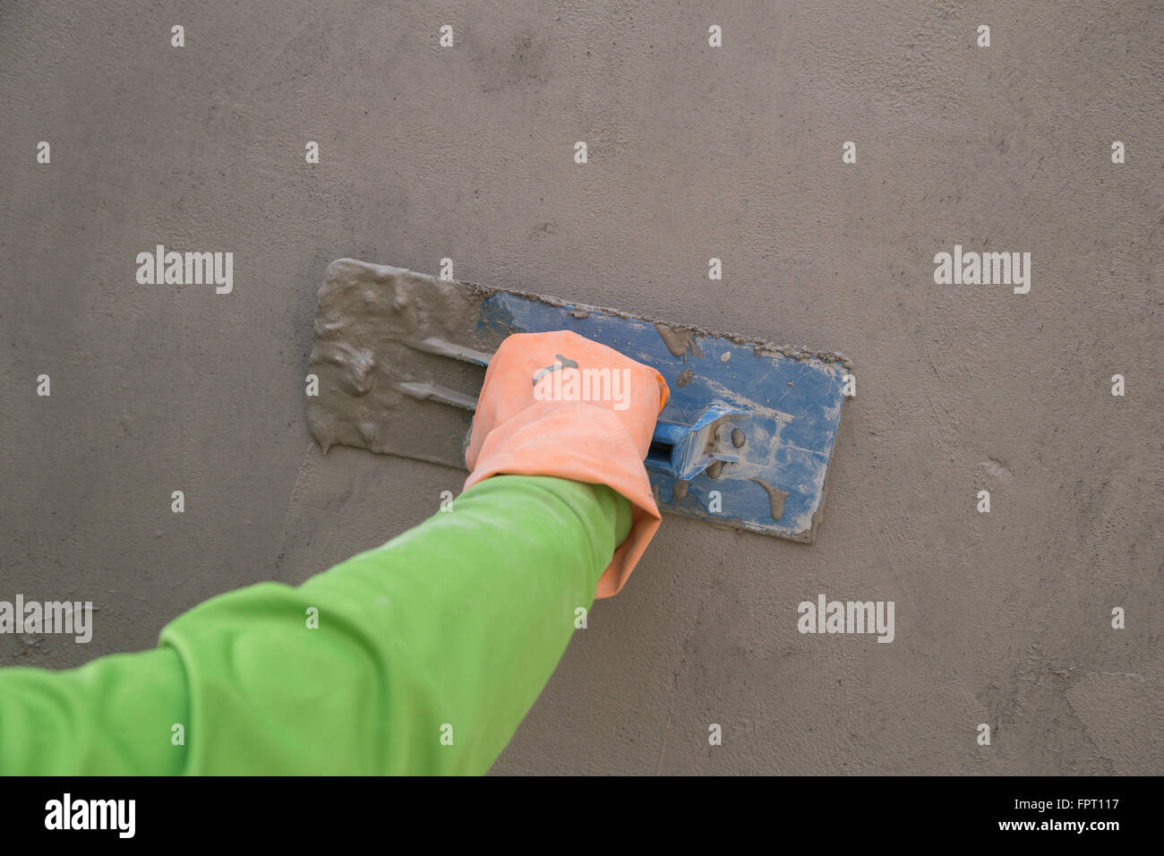 Stretta di mano con cazzuola per finire di calcestruzzo bagnato muro al sito in costruzione Foto Stock