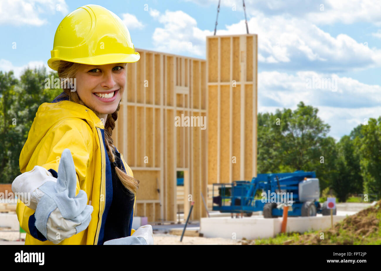 Giovane donna su un sito di costruzione con il pollice verso l'alto. Sullo sfondo di un legno edificio prefabbricato Foto Stock