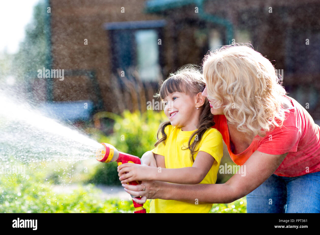 Piccolo giardiniere ragazza con irrigazione madre sul prato vicino casa Foto Stock