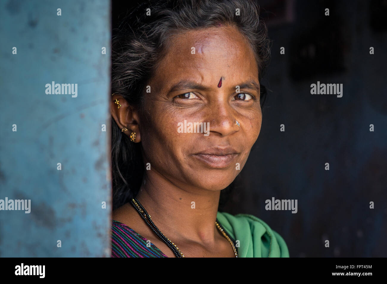 Eleganti donna indiana vestito in verde sari cercando rond una parete blu fuori casa rurale Foto Stock