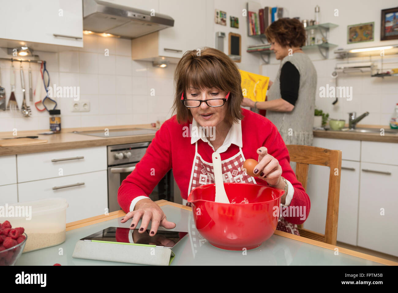Senior donna che cerca ricetta su tavoletta digitale per la torta, Monaco di Baviera, Germania Foto Stock