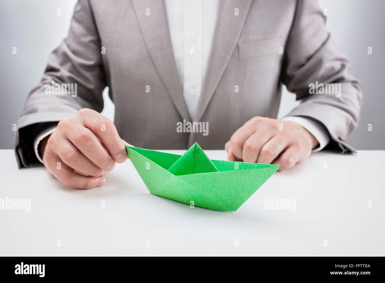 Imprenditore alla scrivania con un libro verde origami barca, concetto di aspirazioni, leadership, strategia o semplicemente la noia in ufficio Foto Stock