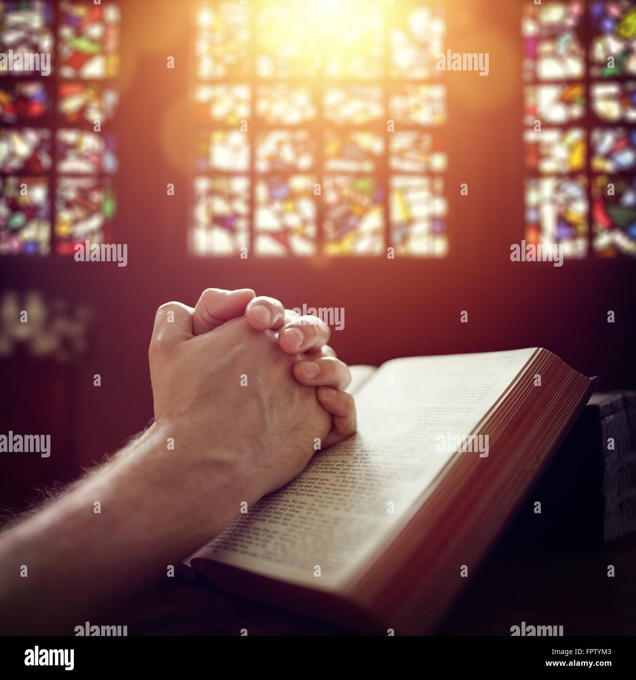 Mani giunte in preghiera in una Sacra Bibbia in una chiesa Foto Stock