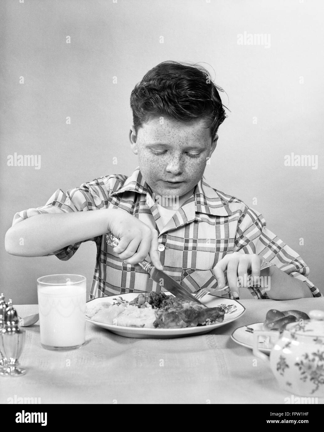 Anni Cinquanta BOY mangiare carne di taglio con il coltello bicchiere di latte Foto Stock