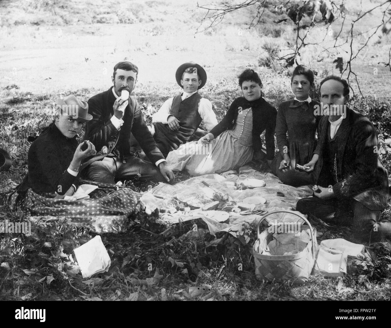 1890s 1900 gruppo di sei persone sedute intorno ad un picnic esterno sparso sulla terra guardando la fotocamera Foto Stock