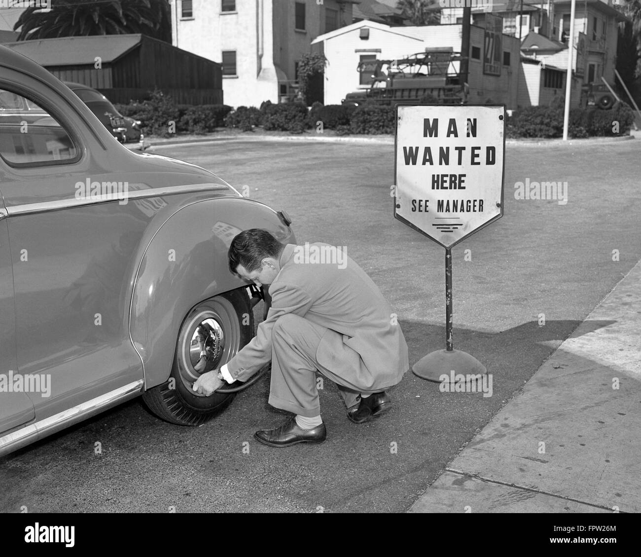 Anni Cinquanta uomo indossare tuta messa aria nel pneumatico automobile accanto all aiuto voluto firmare Foto Stock