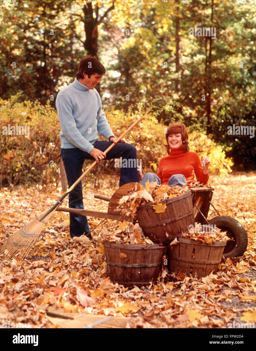 Anni Settanta giovane uomo donna a rastrellare rastrello Foglie di autunno BACKYARD GIARDINAGGIO CANTIERE COPPIE DI LAVORO UOMINI DONNE Foto Stock