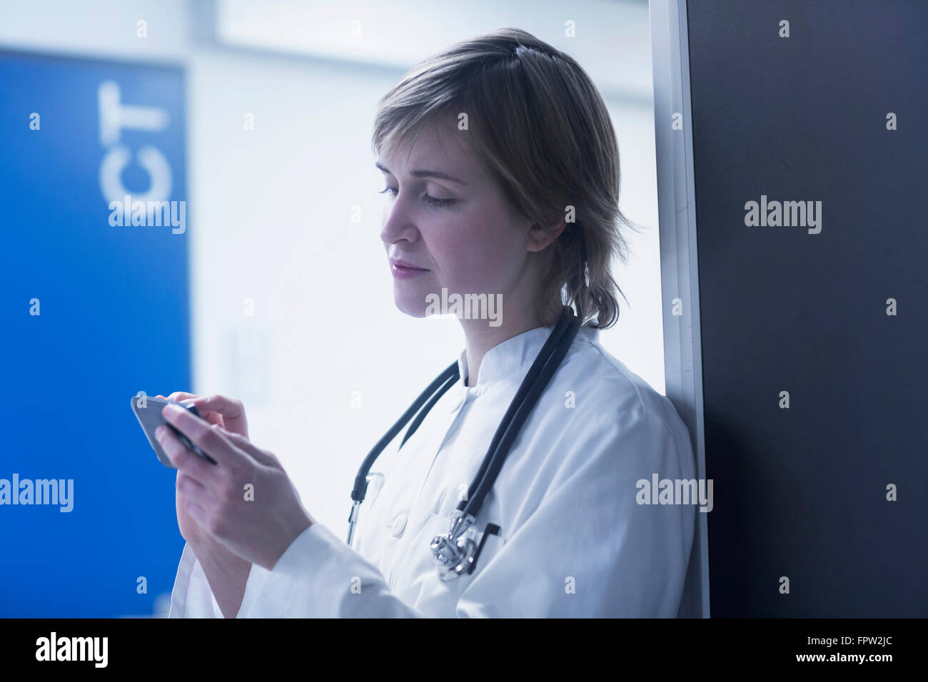 Giovani donne medico di messaggistica di testo sul telefono cellulare in clinica, Freiburg im Breisgau, Baden-Württemberg, Germania Foto Stock