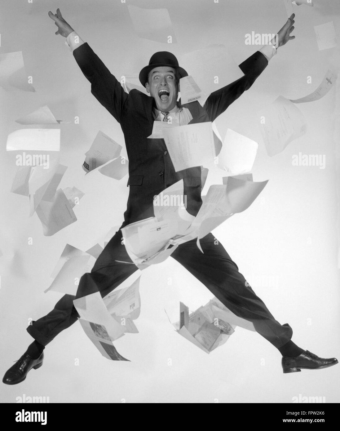 Anni Cinquanta anni sessanta uomo felice venditore imprenditore SUIT TIE HAT saltare in aria le carte Flying tutto guardando la fotocamera Foto Stock