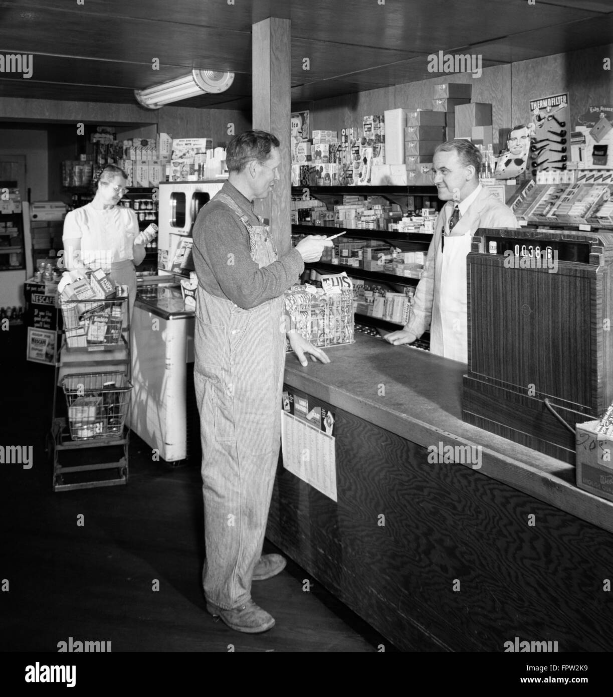 Anni Cinquanta uomo agricoltore al generale rurale MERCANTILE CONTATORE DEL NEGOZIO DI PARLARE AL CANCELLIERE STORE KEEPER AL REGISTRATORE DI CASSA Foto Stock