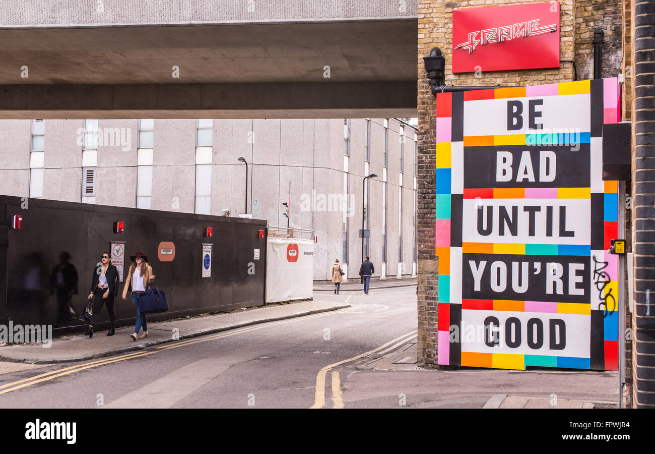 Due ragazze tanga camminare al fianco di un grande tabellone colorato con le parole 'essere male fino a quando non stai bene'. Foto Stock