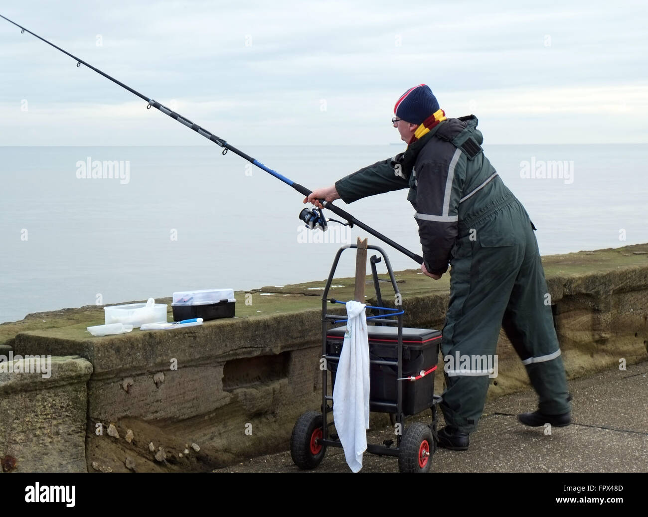 L'uomo della pesca in mare dalla parete del porto. Foto Stock