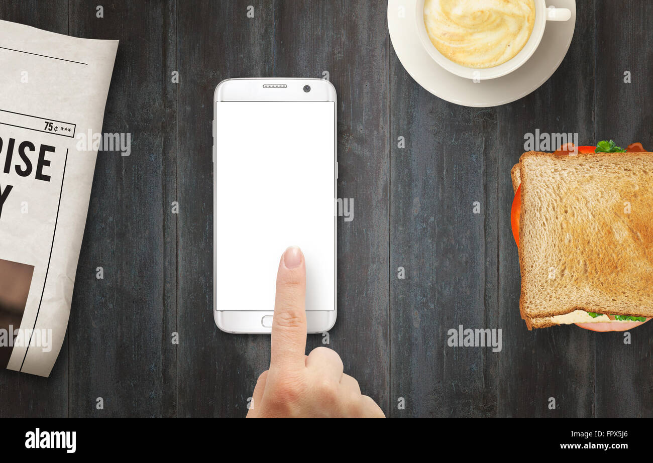 Smart Phone con display isolato per mockup. La mano di toccare il display. Quotidiano, caffè e sandwich sul tavolo. Vista dall'alto. Foto Stock