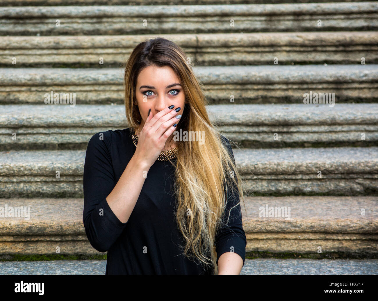 Bella donna con capelli lunghi che coprono la bocca in stato di shock mentre staring a telecamera con stupore Foto Stock